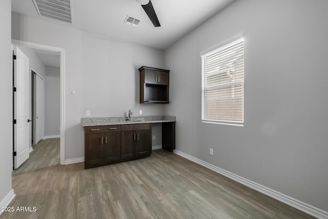 bar featuring ceiling fan, light hardwood / wood-style floors, sink, dark brown cabinetry, and light stone countertops