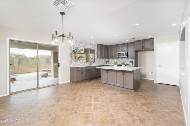 kitchen with a kitchen island, decorative light fixtures, an inviting chandelier, tasteful backsplash, and sink