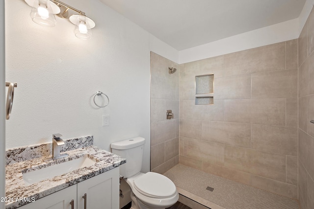 bathroom with toilet, tiled shower, and vanity