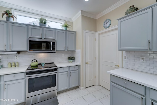 kitchen with light tile patterned flooring, gray cabinets, ornamental molding, and appliances with stainless steel finishes