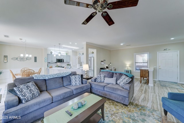 living room with crown molding, ceiling fan with notable chandelier, and light hardwood / wood-style floors