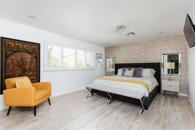 bedroom featuring an accent wall, baseboards, visible vents, and light wood-type flooring