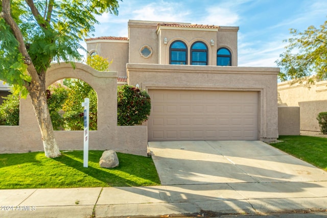 mediterranean / spanish home with concrete driveway, stucco siding, a tile roof, an attached garage, and a front yard