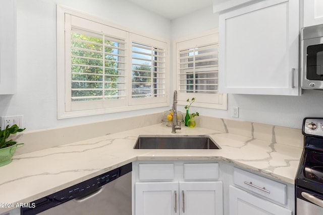 kitchen featuring appliances with stainless steel finishes, white cabinetry, a sink, and light stone counters