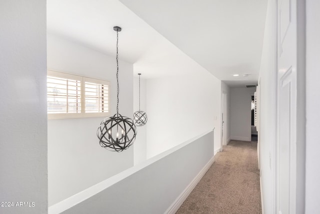 hallway featuring a chandelier, carpet, and baseboards