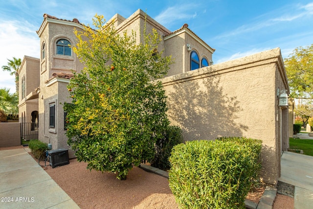 view of side of home with a tile roof, a gate, and stucco siding