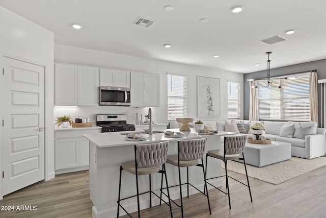 kitchen with sink, hanging light fixtures, light hardwood / wood-style flooring, white cabinets, and appliances with stainless steel finishes