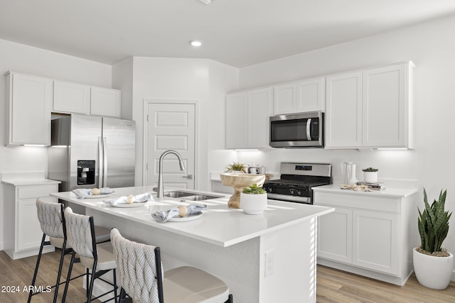 kitchen with stainless steel appliances, sink, light hardwood / wood-style floors, white cabinetry, and an island with sink