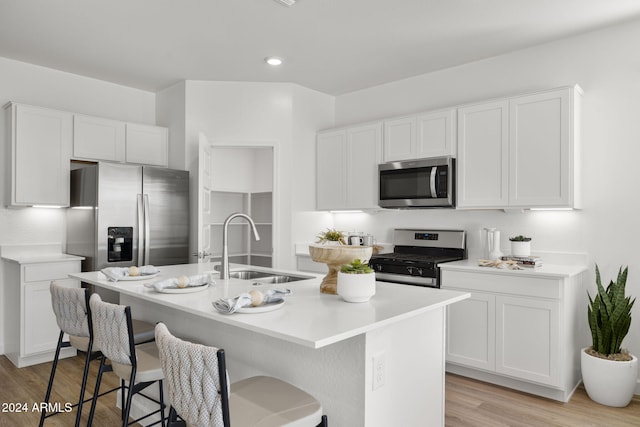 kitchen with a kitchen island with sink, white cabinets, sink, light hardwood / wood-style flooring, and appliances with stainless steel finishes