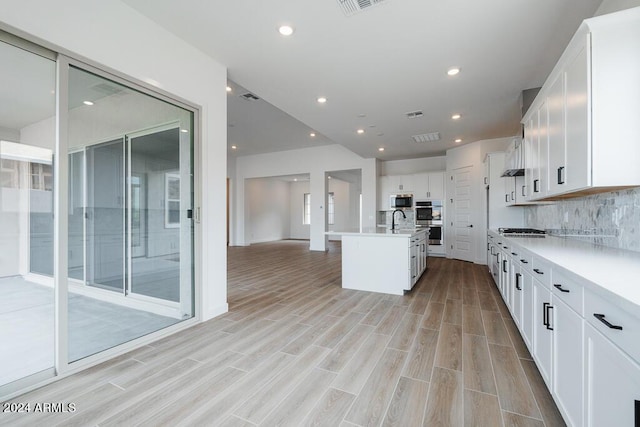 kitchen featuring white cabinetry, stainless steel appliances, sink, backsplash, and a kitchen island with sink