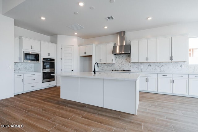 kitchen with white cabinetry, wall chimney exhaust hood, stainless steel appliances, and an island with sink