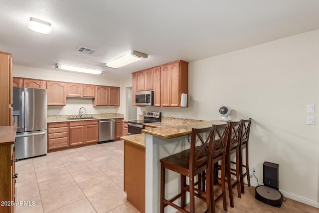 538 E Estevan Ave, Apache Junction, AZ 85119 - kitchen with stainless steel appliances, a peninsula, a kitchen breakfast bar, light tile patterned flooring, and light stone counters