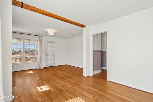 empty room featuring beam ceiling, visible vents, light wood-style flooring, and baseboards