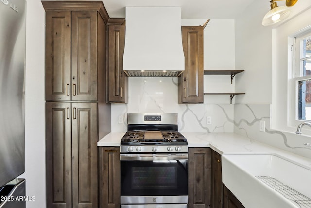 kitchen with light stone counters, decorative backsplash, appliances with stainless steel finishes, a sink, and premium range hood