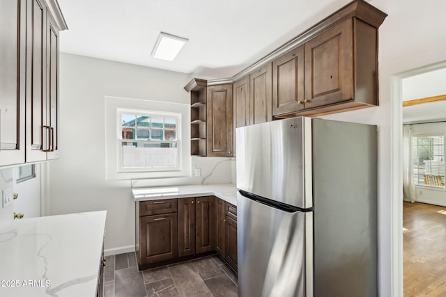 kitchen featuring light stone counters, open shelves, tasteful backsplash, freestanding refrigerator, and dark brown cabinets