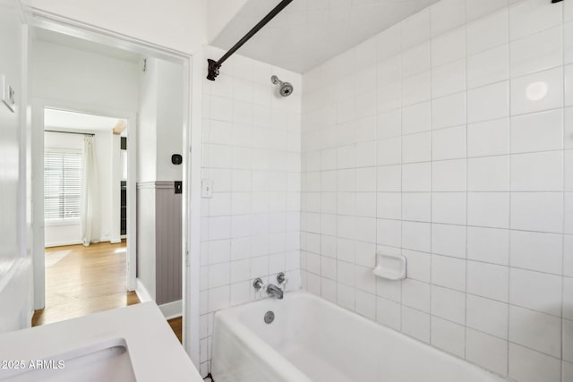 bathroom featuring a wainscoted wall, shower / bath combination, a sink, and wood finished floors