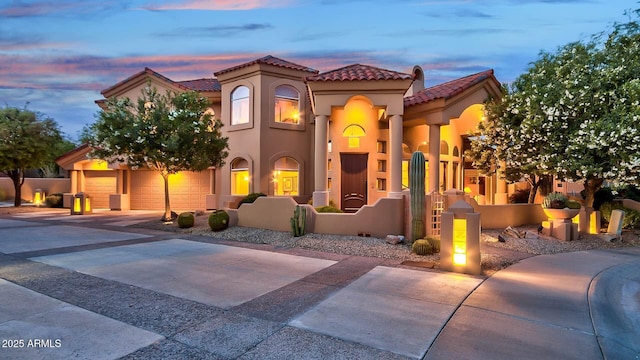 mediterranean / spanish-style home featuring a garage, concrete driveway, a tile roof, and stucco siding