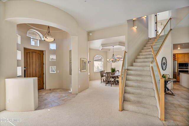 foyer entrance with arched walkways, light colored carpet, a notable chandelier, and stairway