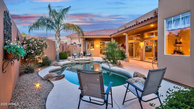 pool at dusk featuring a patio, a fenced in pool, and an in ground hot tub