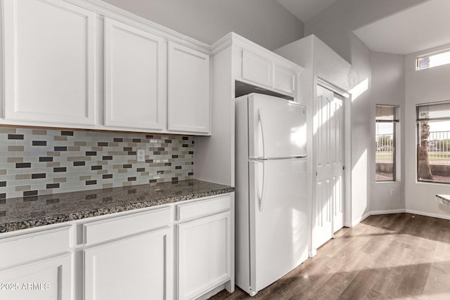 kitchen with white cabinetry, white refrigerator, backsplash, dark stone countertops, and hardwood / wood-style floors