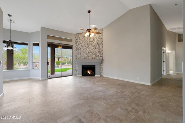 unfurnished living room with high vaulted ceiling, ceiling fan with notable chandelier, a fireplace, baseboards, and visible vents