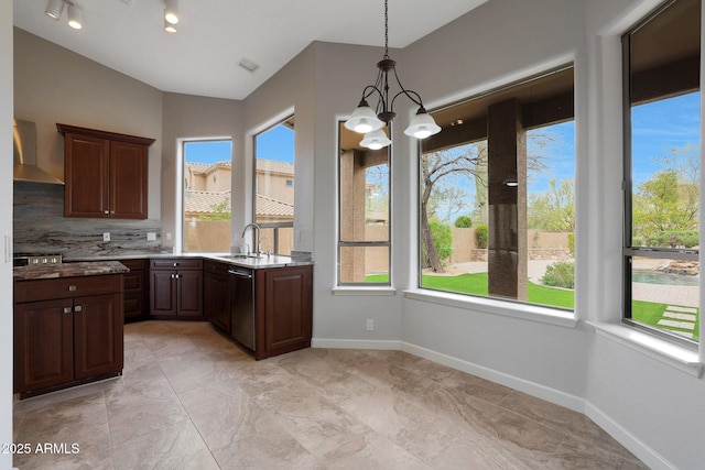 kitchen featuring an inviting chandelier, stainless steel dishwasher, a sink, wall chimney exhaust hood, and pendant lighting
