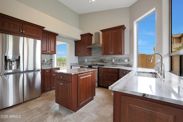 kitchen featuring wall chimney exhaust hood, a sink, backsplash, light stone counters, and appliances with stainless steel finishes