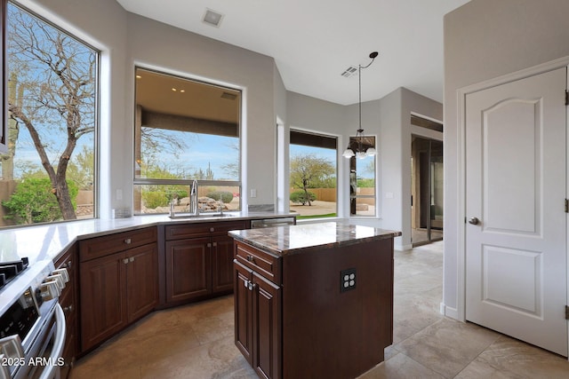 kitchen featuring a sink, stainless steel range, decorative light fixtures, light stone countertops, and visible vents