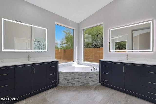 full bathroom featuring two vanities, lofted ceiling, a garden tub, and a sink