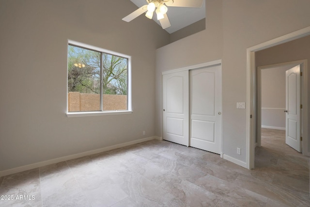 unfurnished bedroom featuring baseboards, a ceiling fan, a towering ceiling, and a closet