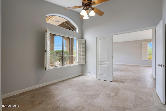 unfurnished room with a ceiling fan, baseboards, and a towering ceiling