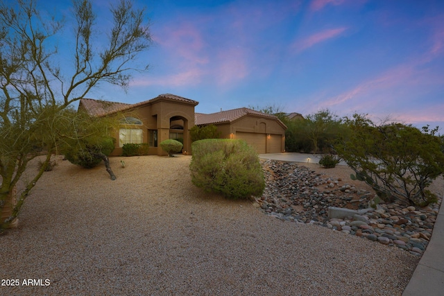 mediterranean / spanish-style house featuring an attached garage, a tiled roof, stucco siding, and driveway