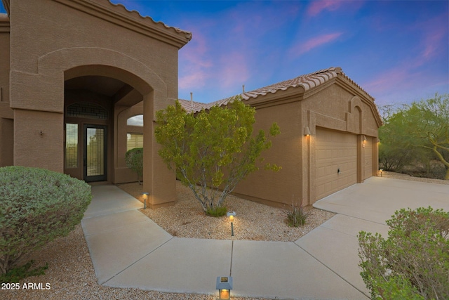 exterior entry at dusk featuring stucco siding, a tile roof, and a garage