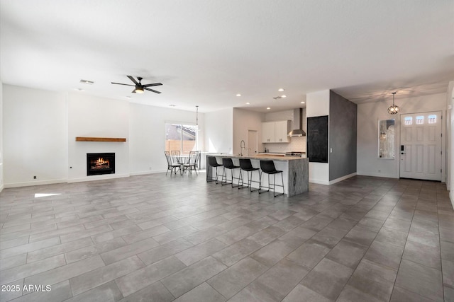 unfurnished living room with a sink, baseboards, a warm lit fireplace, and ceiling fan