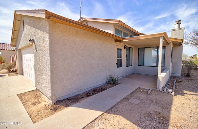 view of side of home featuring driveway, an attached garage, and stucco siding