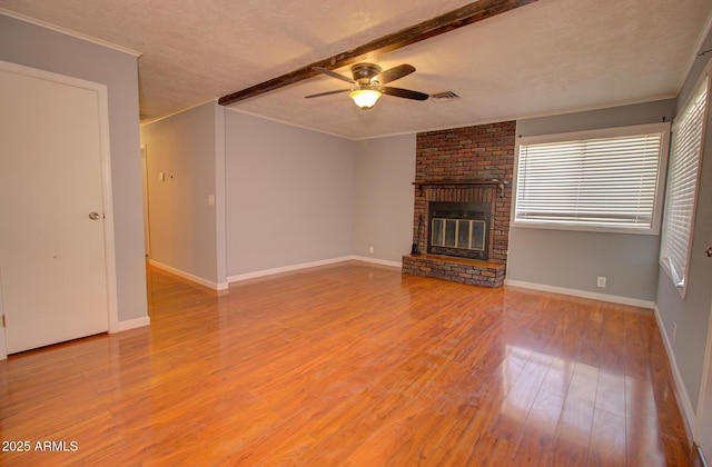 unfurnished living room featuring visible vents, ornamental molding, wood finished floors, a textured ceiling, and a brick fireplace