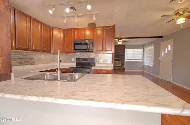 kitchen featuring appliances with stainless steel finishes, brown cabinets, a peninsula, a sink, and backsplash