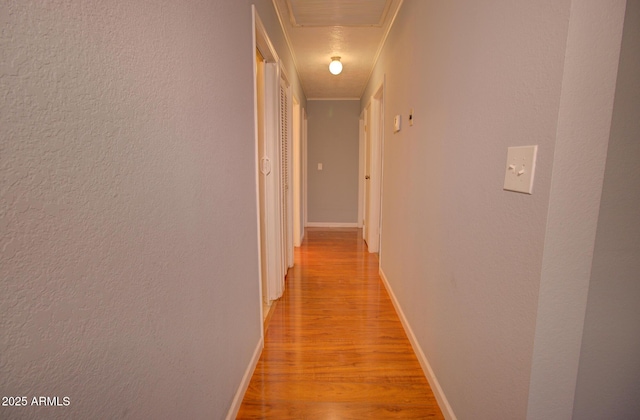 hallway featuring light wood-style flooring, visible vents, baseboards, and a textured wall