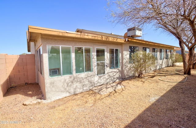 rear view of house featuring central air condition unit, fence, and stucco siding