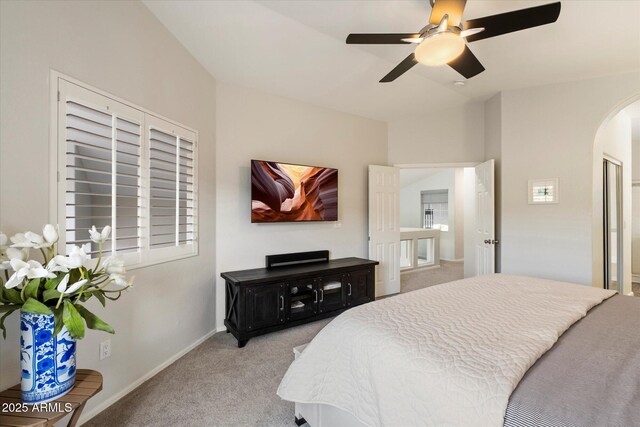 bedroom featuring light colored carpet, arched walkways, baseboards, and a ceiling fan