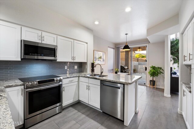 kitchen with stainless steel appliances, a sink, backsplash, a peninsula, and white cabinets
