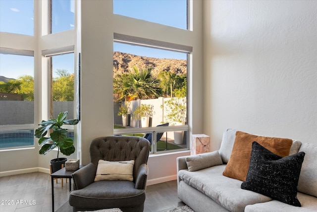 sitting room with healthy amount of natural light, baseboards, a towering ceiling, wood finished floors, and a mountain view