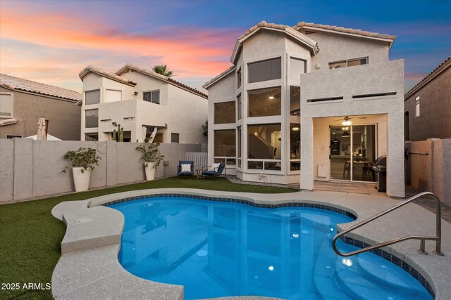 back of house at dusk with fence, stucco siding, a tiled roof, and a patio