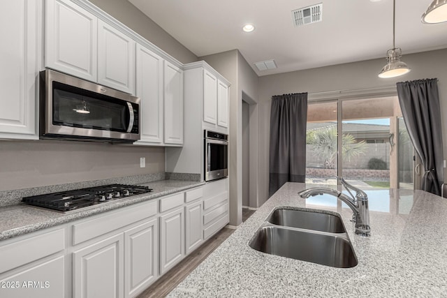 kitchen with appliances with stainless steel finishes, light stone countertops, sink, white cabinetry, and decorative light fixtures