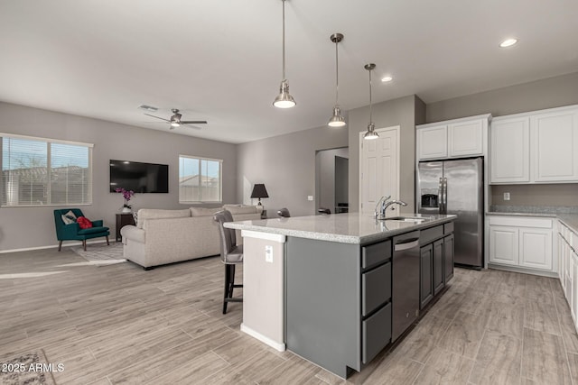 kitchen featuring appliances with stainless steel finishes, an island with sink, sink, white cabinetry, and decorative light fixtures