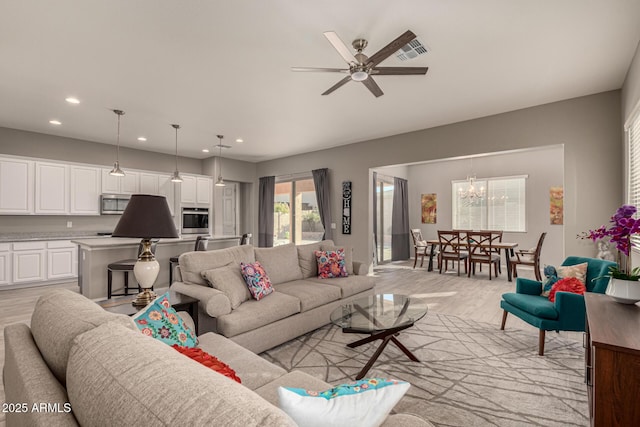 living room featuring ceiling fan with notable chandelier and light wood-type flooring