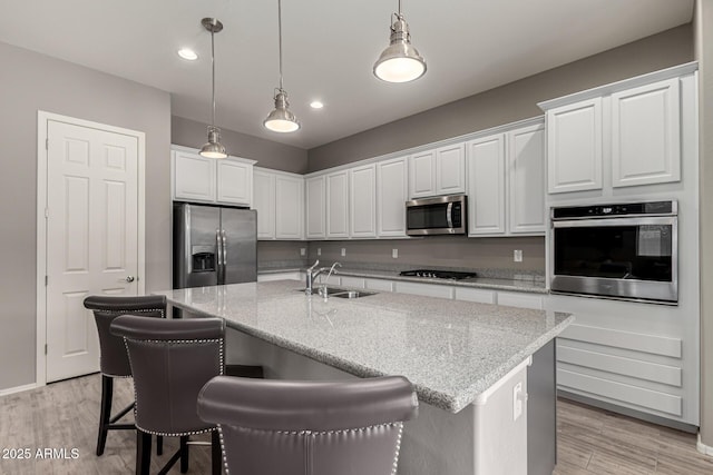 kitchen with appliances with stainless steel finishes, an island with sink, white cabinets, and sink