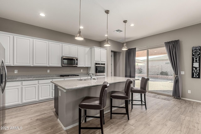 kitchen with stainless steel appliances, an island with sink, white cabinets, decorative light fixtures, and sink