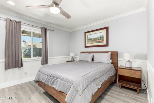 bedroom featuring wood finished floors, ornamental molding, a wainscoted wall, and a ceiling fan