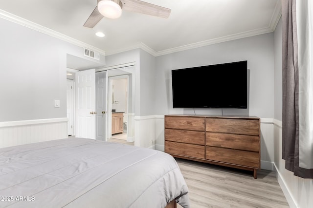 bedroom with crown molding, wainscoting, light wood finished floors, and a ceiling fan